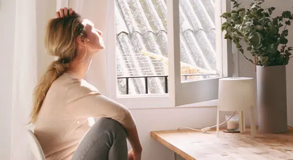 A woman sitting on the floor looking out of a window.